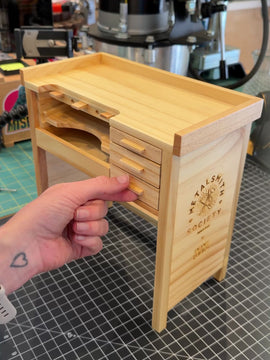 A hand pulls out the drawers on the small wooden jeweler's bench to show its size relative to a human hand.